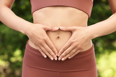 Healthy digestion. Woman making heart shape with hands near her belly outdoors, closeup