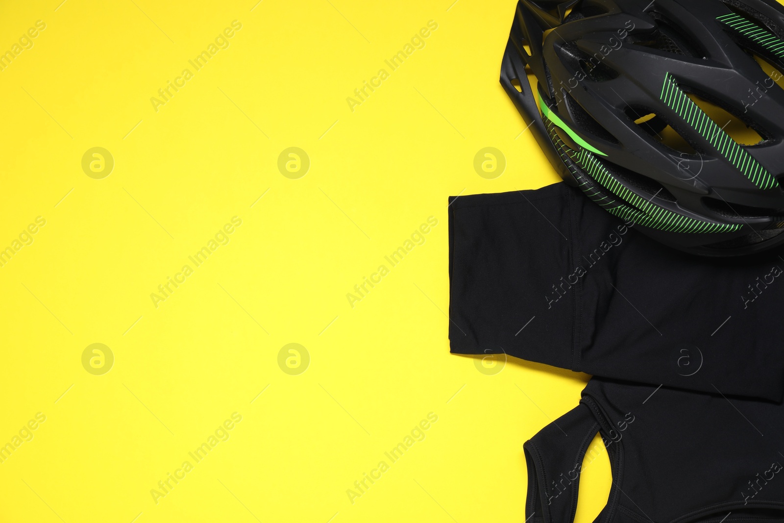 Photo of Bicycle helmet and sportswear on yellow background, flat lay. Space for text