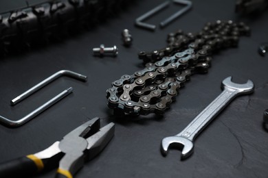 Wrench, pliers, bicycle tire, chain and screws on dark gray textured background, closeup