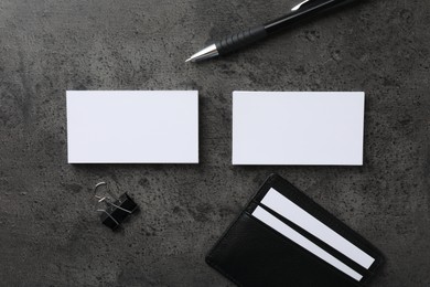 Leather card holder with blank business cards, pen and binder clip on grey textured table, flat lay. Mockup for design