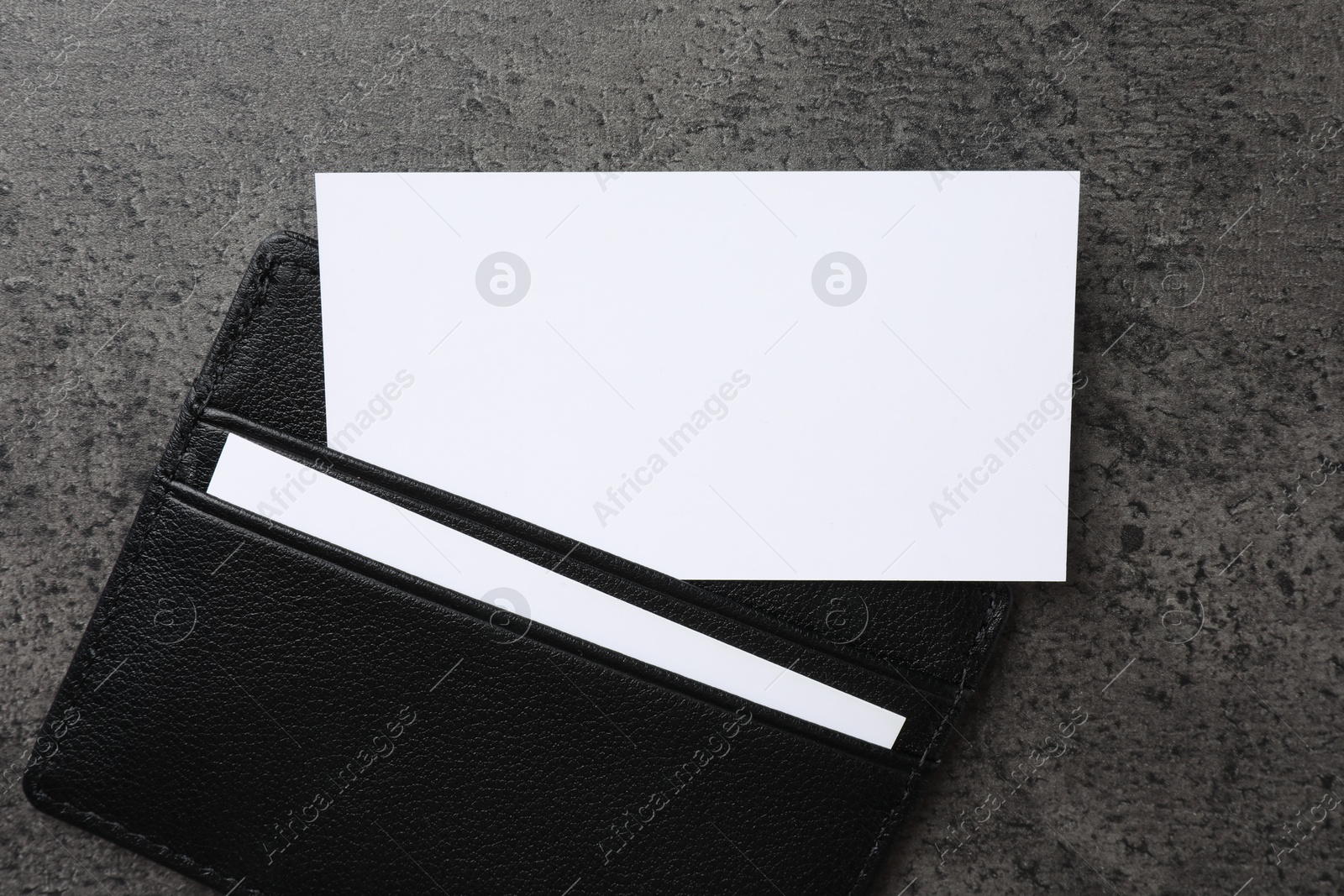 Photo of Leather card holder with blank business cards on grey textured table, top view. Mockup for design