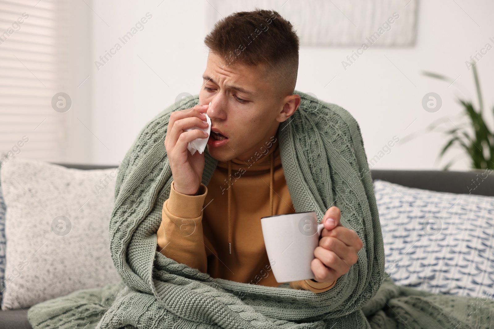 Photo of Cold symptom. Young man with hot tea suffering from fever at home