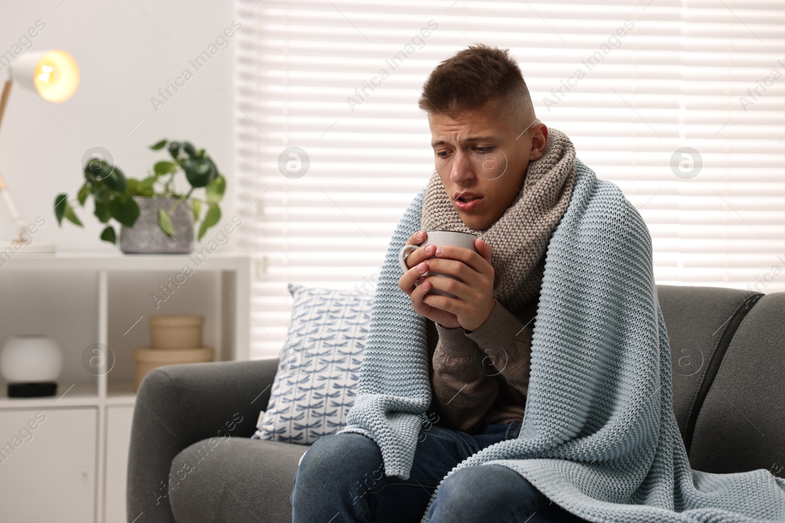 Photo of Cold symptom. Young man with hot tea suffering from fever at home