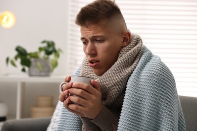 Photo of Cold symptom. Young man with hot tea suffering from fever at home