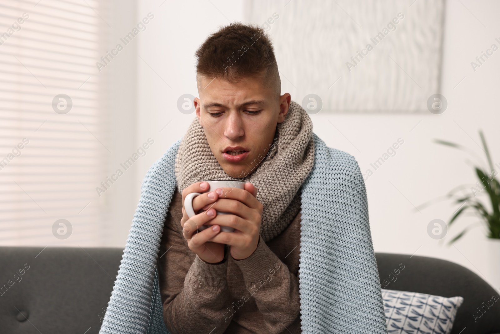 Photo of Cold symptom. Young man with hot tea suffering from fever at home