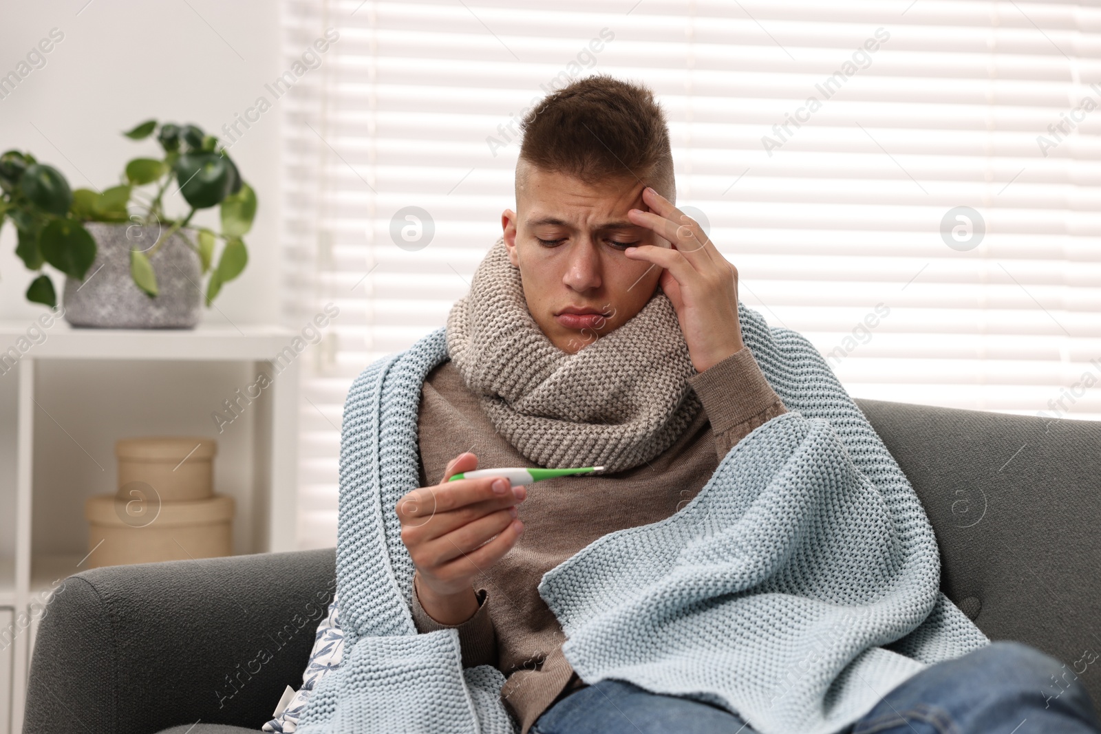 Photo of Cold symptom. Young man checking temperature with thermometer at home