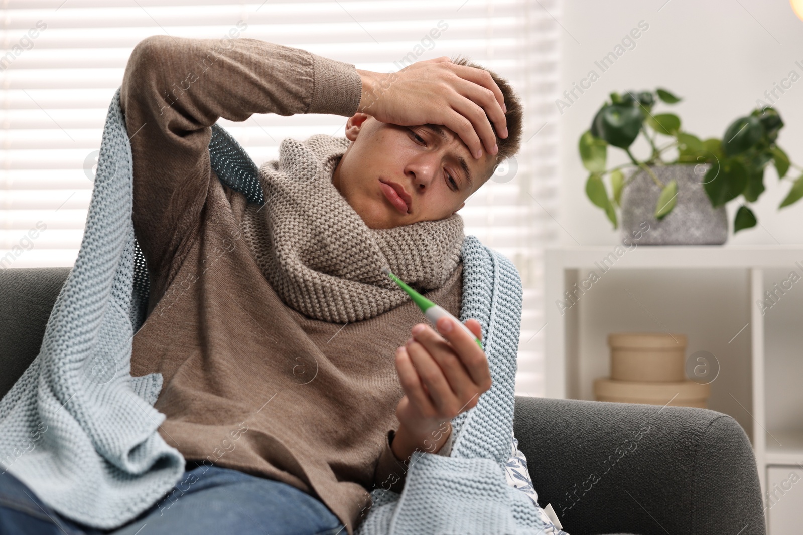 Photo of Cold symptom. Young man checking temperature with thermometer at home