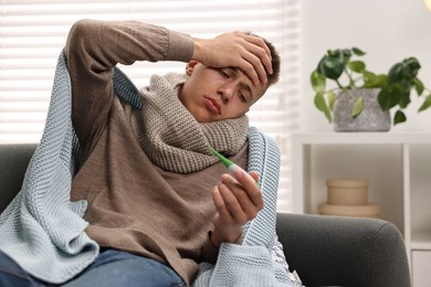 Photo of Cold symptom. Young man checking temperature with thermometer at home