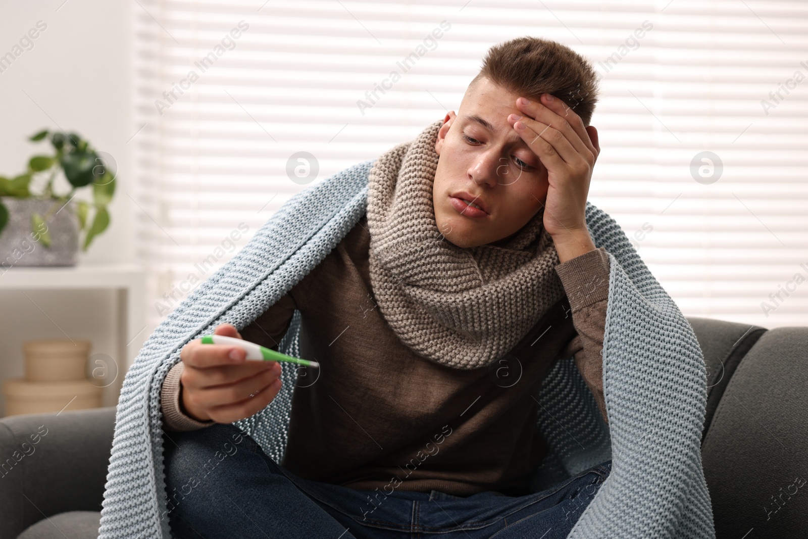 Photo of Cold symptom. Young man checking temperature with thermometer at home