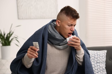 Photo of Cold symptom. Young man with pills coughing at home