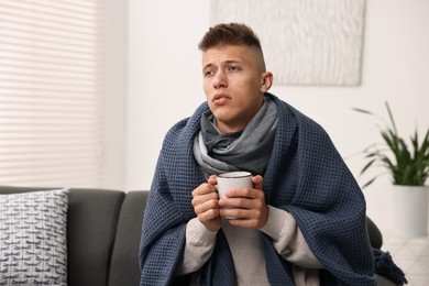 Photo of Cold symptom. Young man with hot tea suffering from fever at home