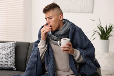Photo of Cold symptom. Young man with hot tea coughing at home