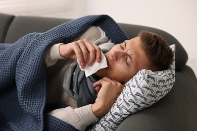 Photo of Cold symptom. Young man suffering from fever on sofa at home