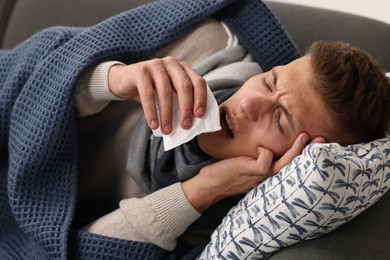 Photo of Cold symptom. Young man with runny nose on sofa at home