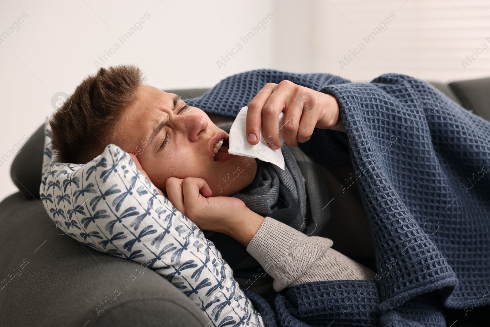 Photo of Cold symptom. Young man with runny nose on sofa at home