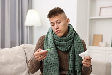 Photo of Cold symptom. Young man checking temperature with thermometer at home