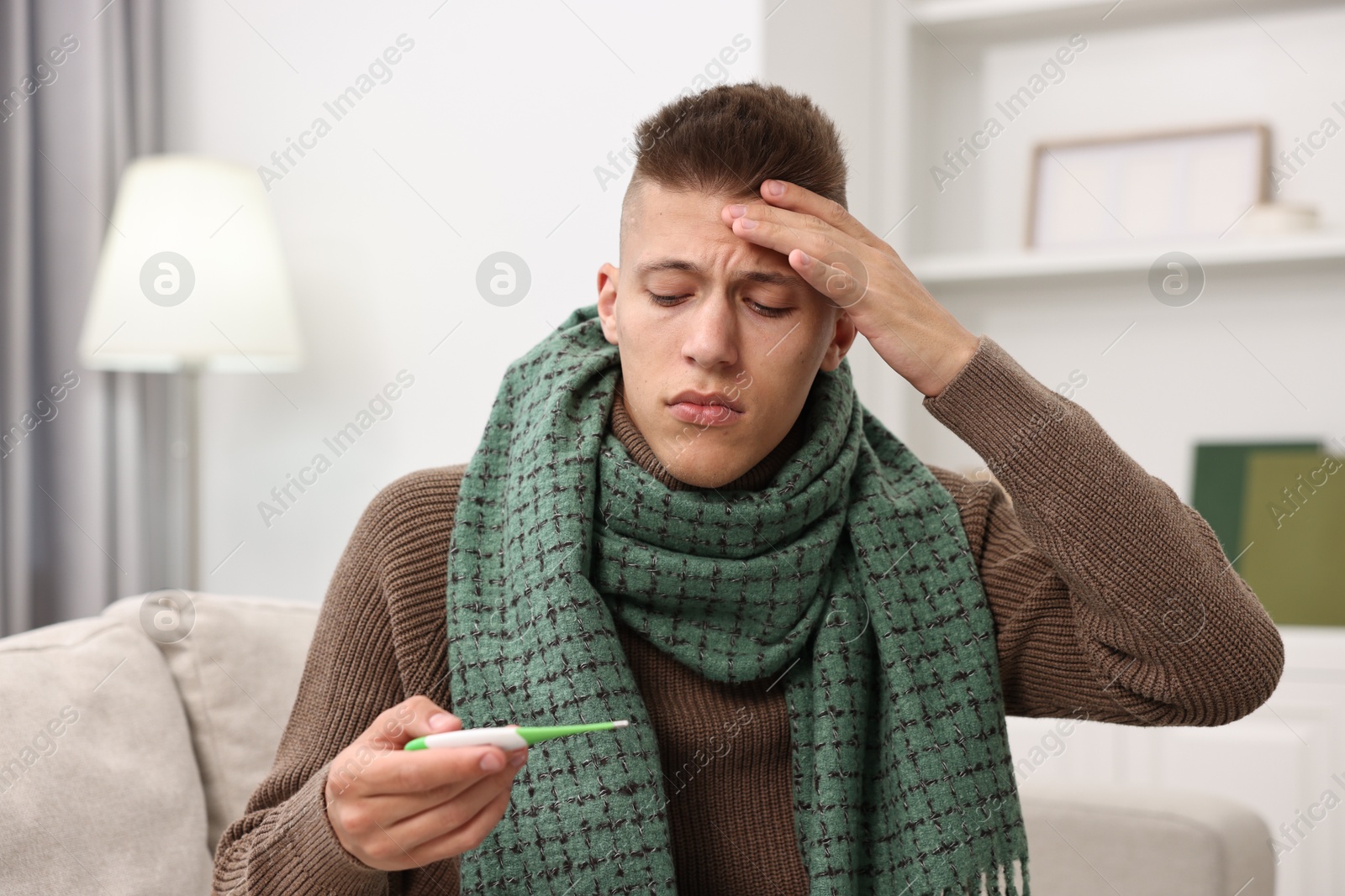 Photo of Cold symptom. Young man checking temperature with thermometer at home