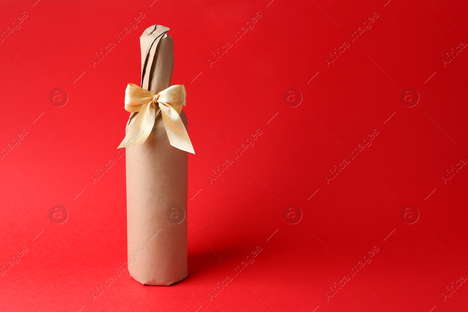 Photo of Wine packed bottle with ribbon on red background, space for text