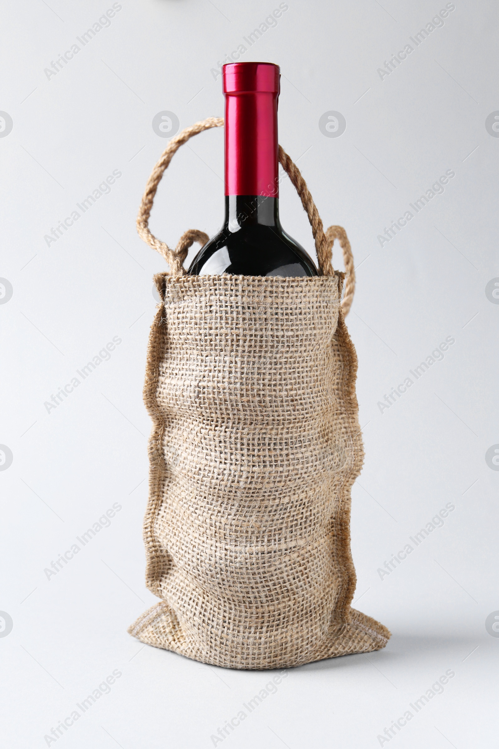 Photo of Wine bottle in burlap bag on light grey background