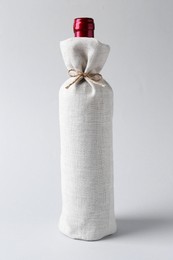 Photo of Wine bottle in burlap package on light grey background