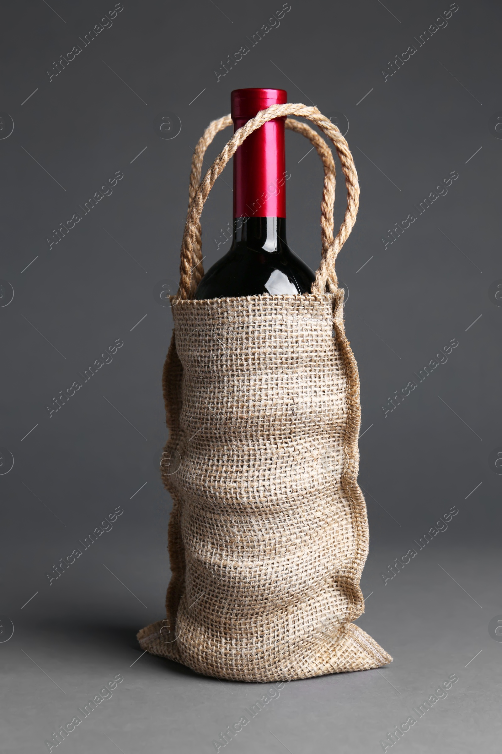 Photo of Wine bottle in burlap bag on grey background