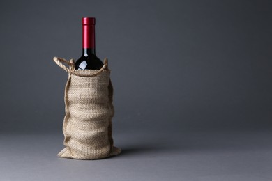 Photo of Wine bottle in burlap bag on grey background, space for text