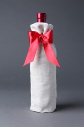 Photo of Wine bottle in burlap package with red ribbon on grey background