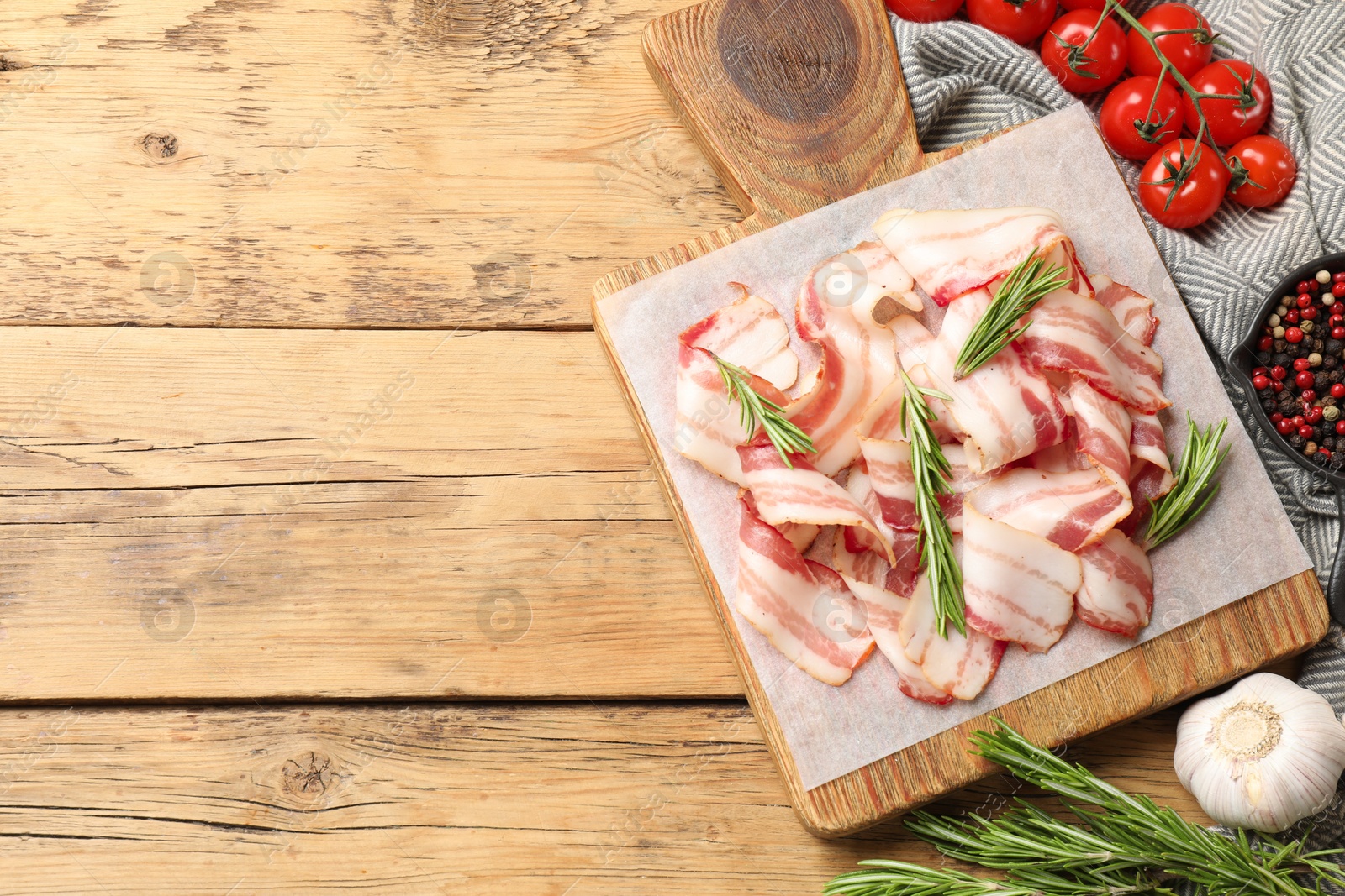 Photo of Slices of raw bacon, spices and tomatoes on wooden table, flat lay. Space for text