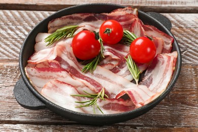 Delicious bacon slices, spices and cherry tomatoes in frying pan on wooden table, closeup