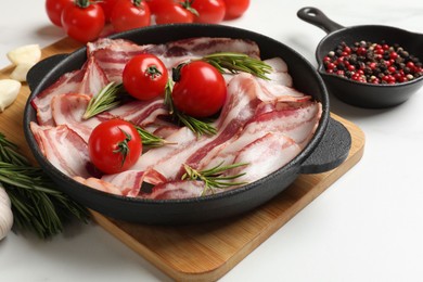 Photo of Delicious bacon slices in frying pan, spices and tomatoes on white table