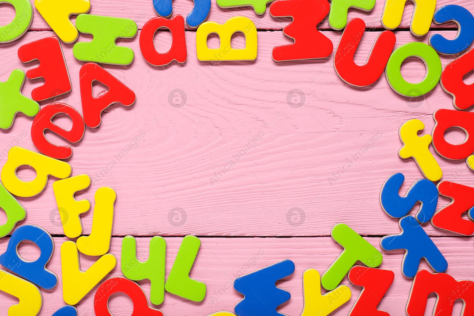 Photo of Learning alphabet. Frame made of magnetic letters on pink wooden background, top view. Space for text