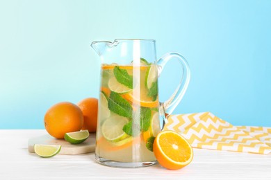 Photo of Freshly made lemonade with mint in jug on white wooden table against light blue background