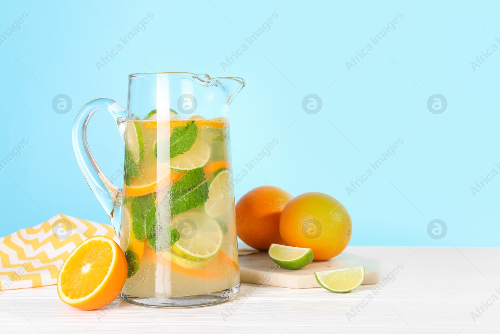 Photo of Freshly made lemonade with mint in jug on white wooden table against light blue background, space for text