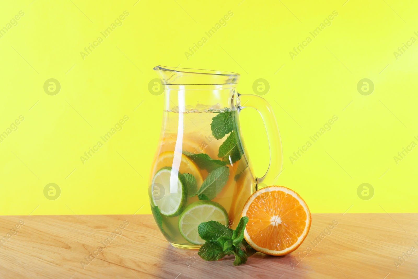 Photo of Freshly made lemonade with mint in jug on wooden table against yellow background