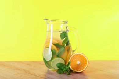 Photo of Freshly made lemonade with mint in jug on wooden table against yellow background