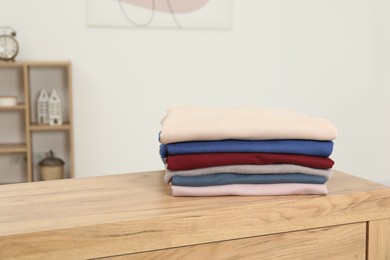 Stack of clothes on wooden chest of drawers indoors, space for text