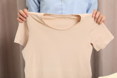 Woman holding clean beige t-shirt indoors, closeup