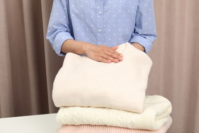 Photo of Woman folding clothes at white table indoors, closeup