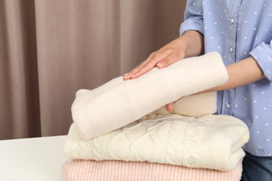 Photo of Woman folding clothes at white table indoors, closeup