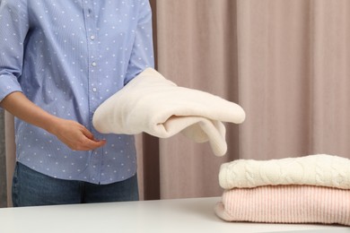 Woman folding clothes at white table indoors, closeup