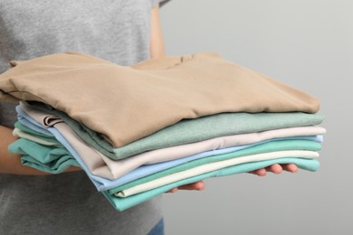 Woman with stack of clothes on grey background, closeup