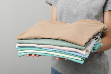 Photo of Woman with stack of clothes on grey background, closeup