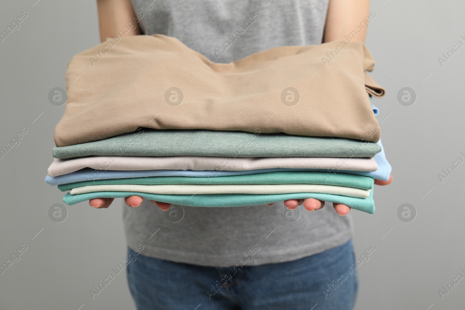 Photo of Woman with stack of clothes on grey background, closeup