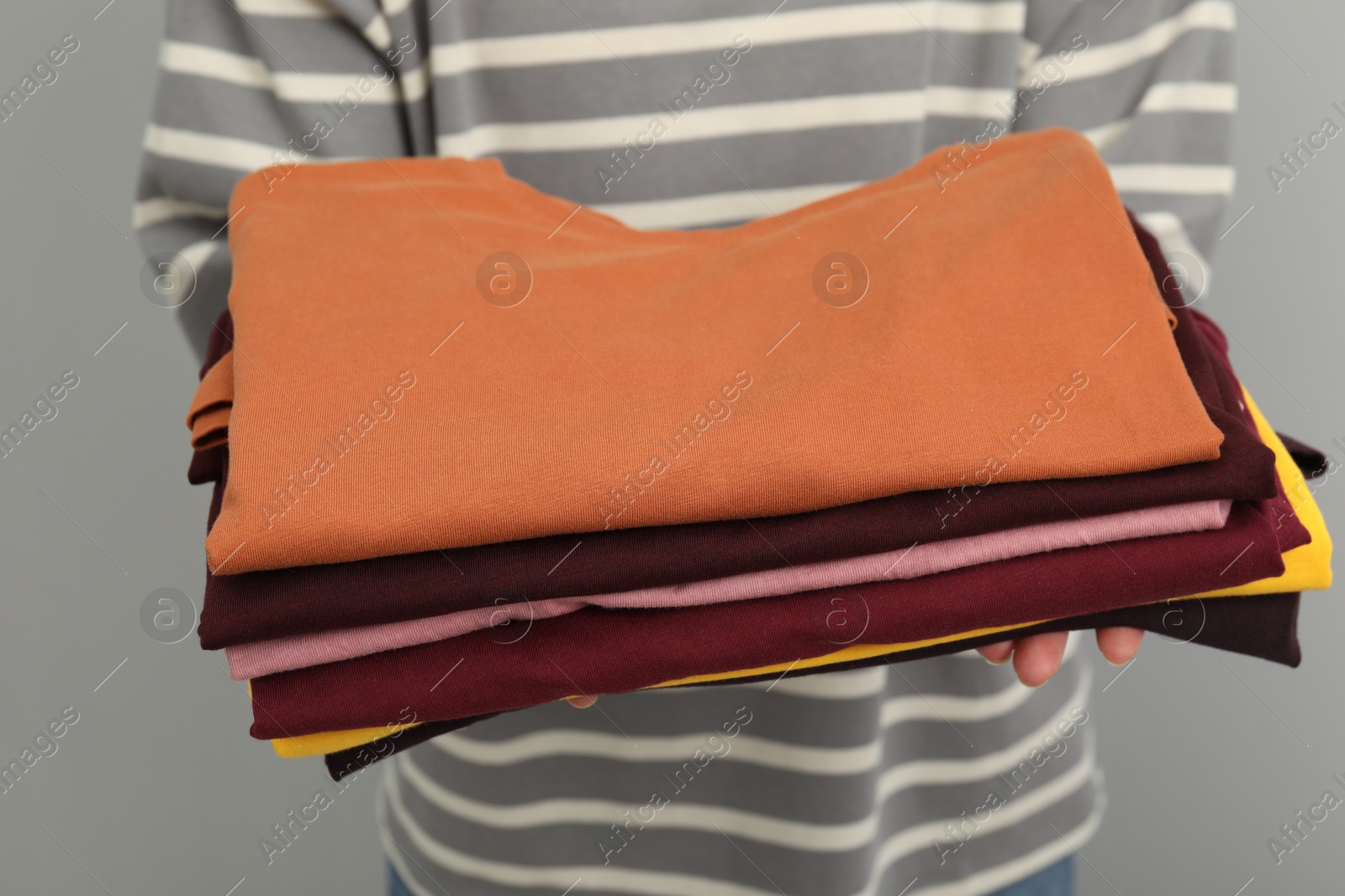 Photo of Woman with stack of clothes on grey background, closeup