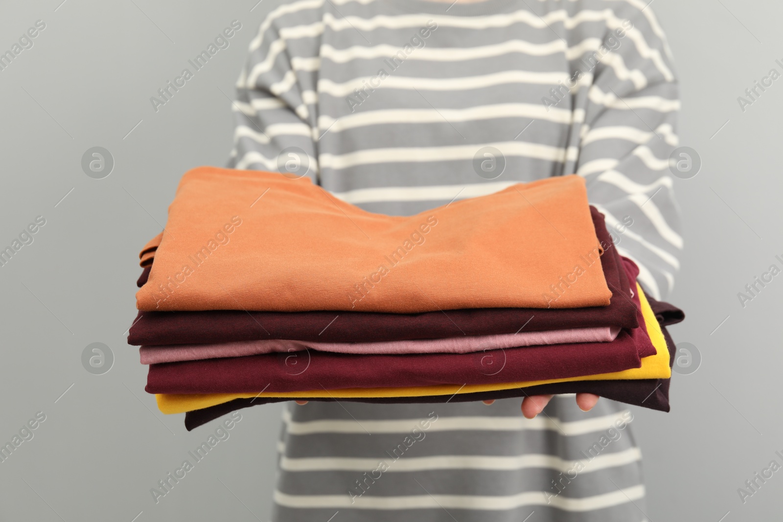 Photo of Woman with stack of clothes on grey background, closeup