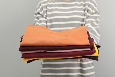 Woman with stack of clothes on grey background, closeup