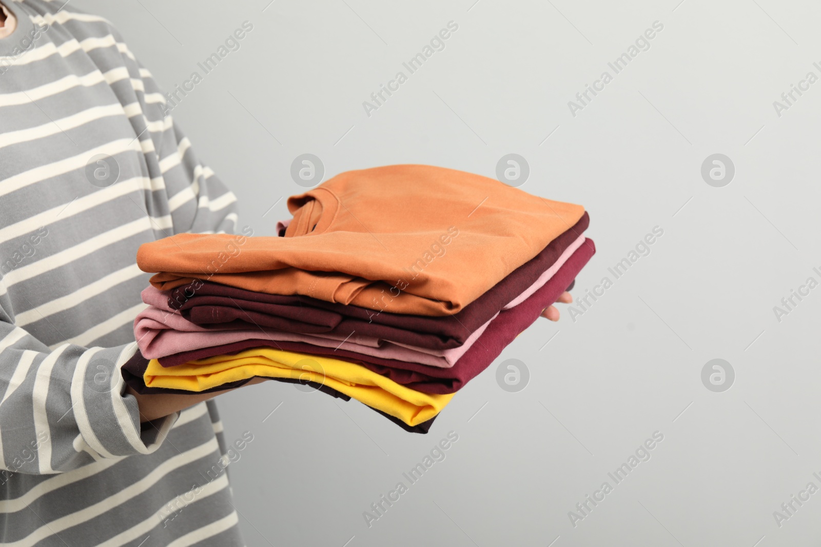 Photo of Woman with stack of clothes on grey background, closeup. Space for text