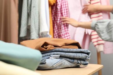 Woman choosing outfit near rack indoors, focus on stack of clothes