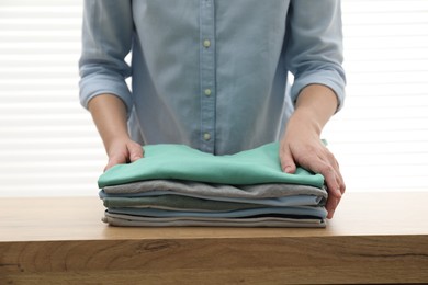 Woman stacking clean clothes at wooden table indoors, closeup