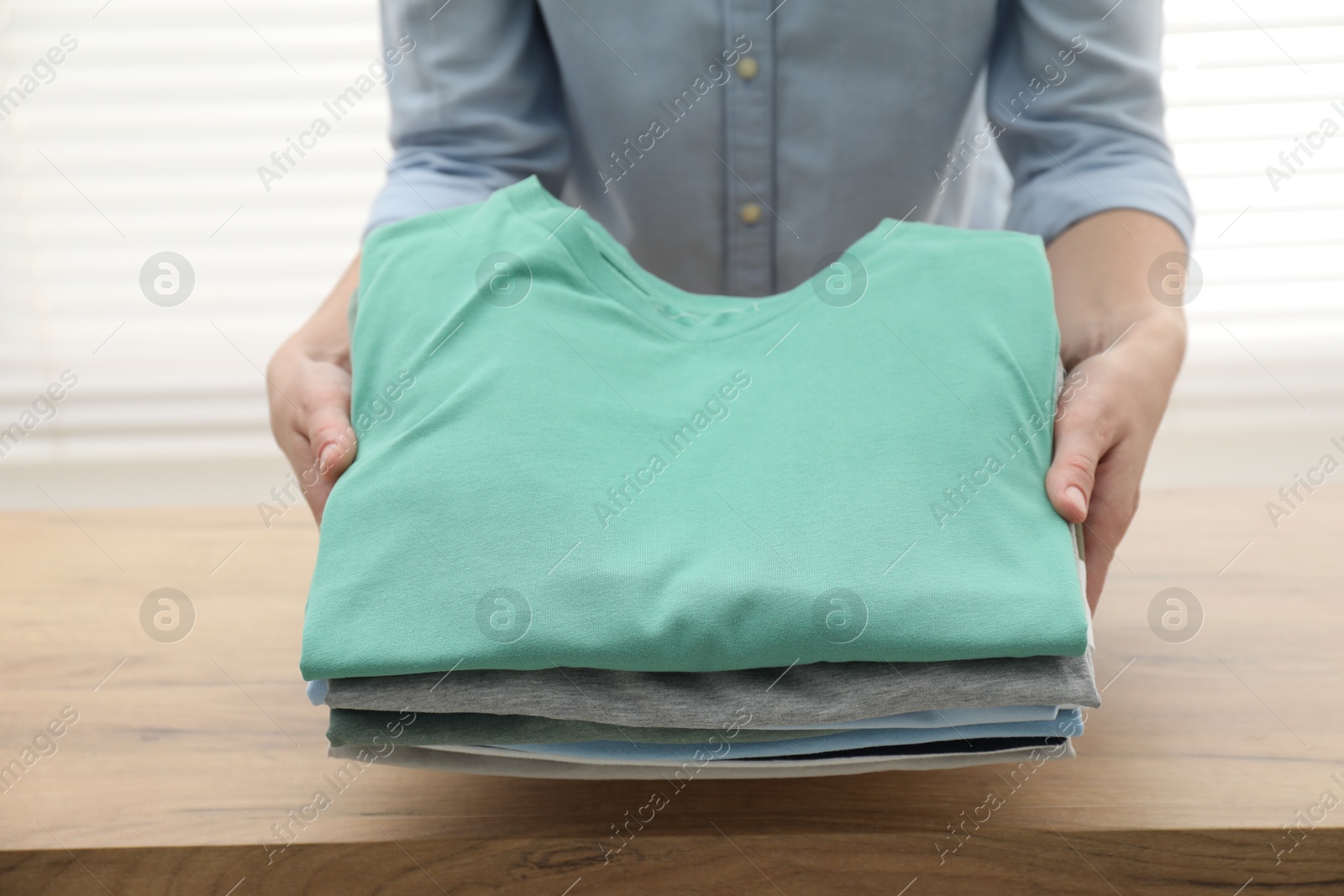 Photo of Woman stacking clean clothes at wooden table indoors, closeup